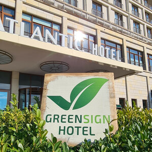 Fassade eines modernen Hotels mit "Greensign Hotel"-Schild und grünen Pflanzen im Vordergrund.