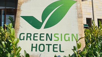 Fassade eines modernen Hotels mit "Greensign Hotel"-Schild und grünen Pflanzen im Vordergrund.
