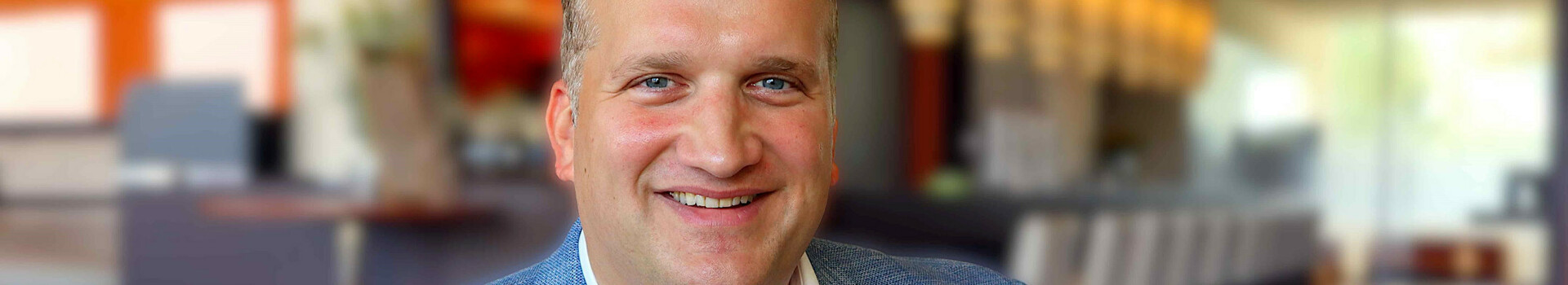 A smiling man in a blue jacket sits in a stylish hotel lobby.