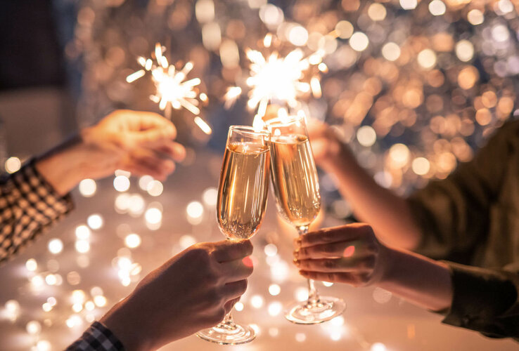People toast with champagne glasses, surrounded by sparklers and twinkling lights.