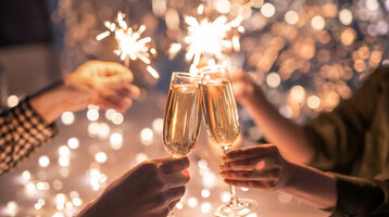 People toast with champagne glasses, surrounded by sparklers and twinkling lights.