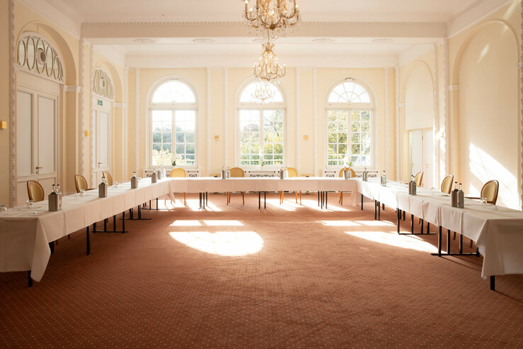 Heller Tagungsraum im ATLANTIC Grand Hotel Travemünde mit U-förmiger Tischanordnung, eleganten Stühlen und großen Fenstern.