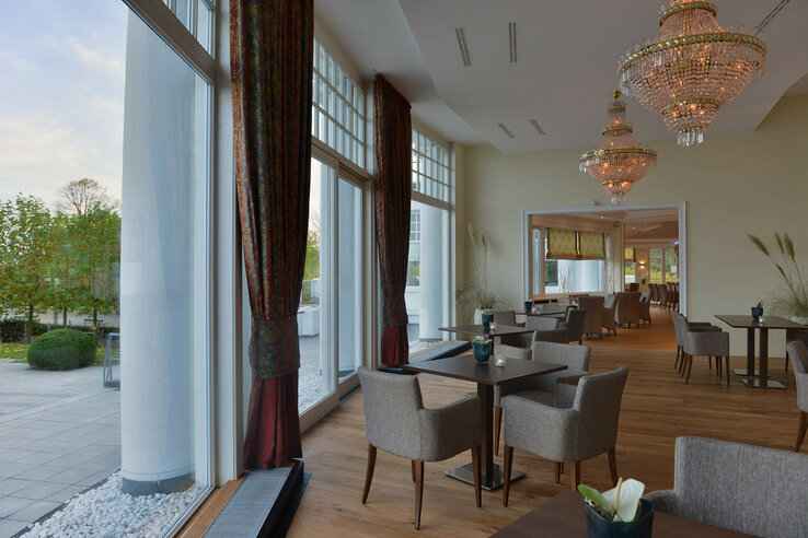 Helles Hotelrestaurant mit großen Fenstern, eleganten Kronleuchtern und stilvoll gedeckten Tischen.