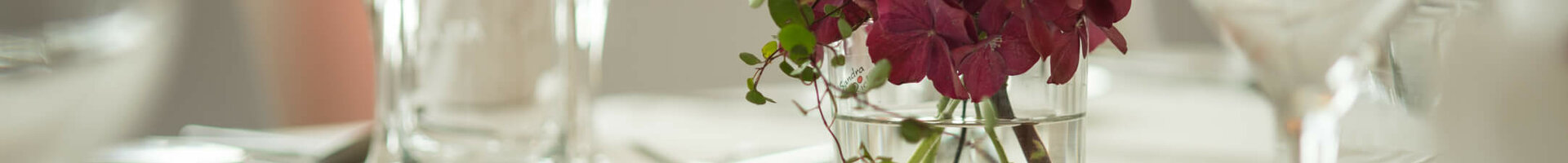 Elegante Tischdekoration im ATLANTIC Hotel Kiel mit Blumenarrangement und Gläsern auf weißer Tischdecke.