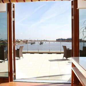 Helle Terrasse mit Blick aufs Wasser, modernen Möbeln und Pflanzen im Vordergrund.