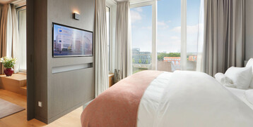 Bright hotel room with large bed, TV and floor-to-ceiling windows with a view of the city at the ATLANTIC Grand Hotel Bremen.