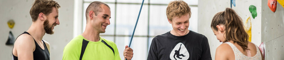 Gruppe von vier Personen beim Indoor-Klettern, lachend und in Kletterausrüstung an einer Kletterwand.