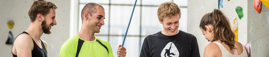 Group of four people indoor climbing, laughing and wearing climbing gear on a climbing wall.