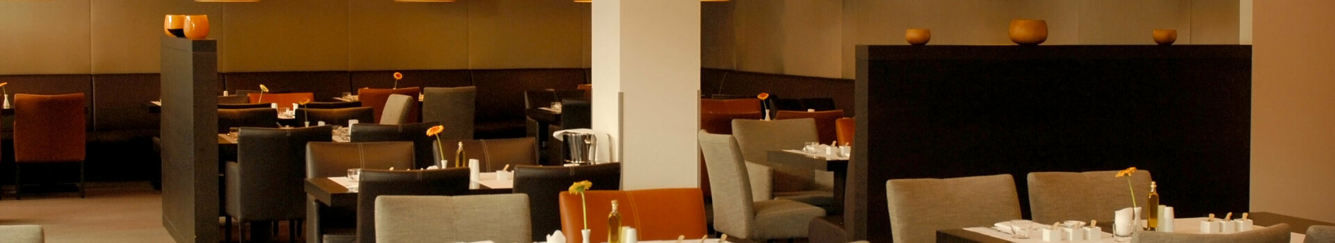 Modern hotel restaurant with elegantly laid tables, comfortable chairs and warm lighting at the ATLANTIC Hotel Lübeck.