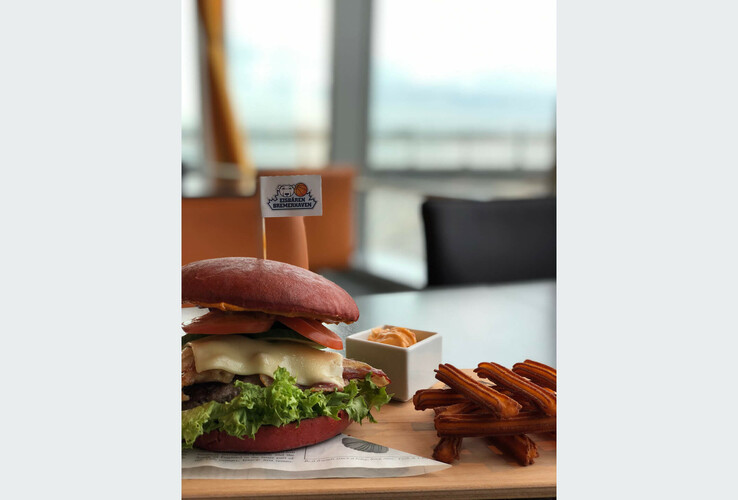 Burger with a red bun and fries on a wooden board at the ATLANTIC Hotel Sail City Restaurant in Bremerhaven.