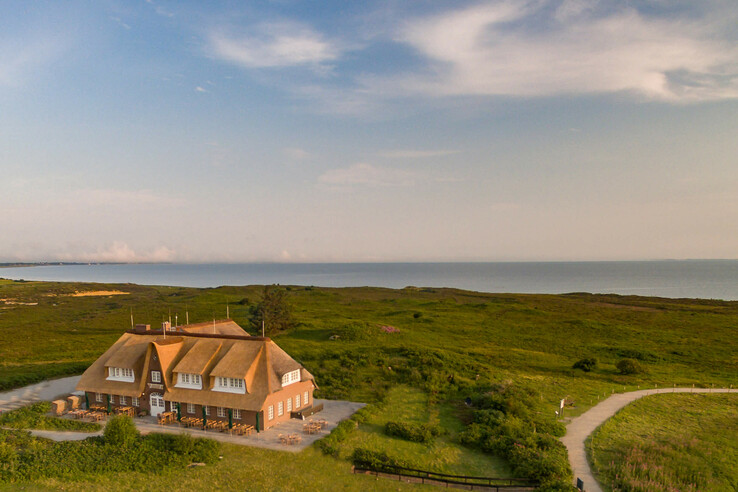 Thatched Hotel Landhaus Severin*s on Sylt, surrounded by green countryside, with a view of the sea.