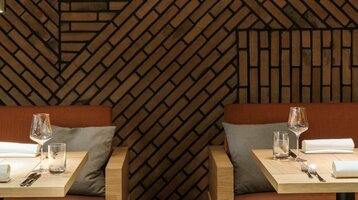 Elegantes Restaurant mit gemusterten Backsteinwänden, gedeckten Tischen, orangefarbenen Polstern und stilvoller Beleuchtung.