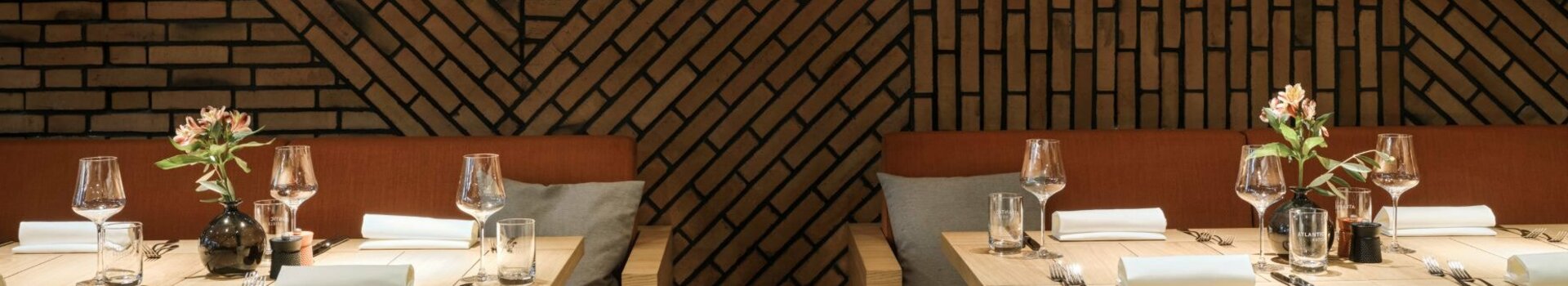 Elegant restaurant with patterned brick walls, laid tables, orange upholstery and stylish lighting.