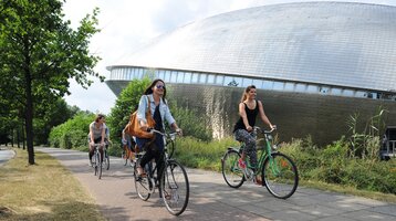 Personen fahren Fahrrad in der Nähe vom Universum Bremen, umgeben von grüner Natur.