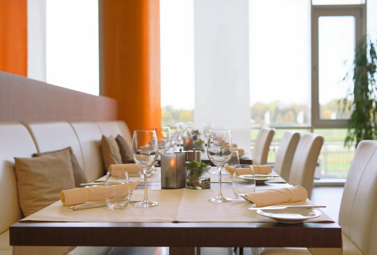 Modernes Restaurant mit elegant gedeckten Tischen, weißen Stühlen und großen Fenstern im ATLANTIC Hotel Galopprennbahn.