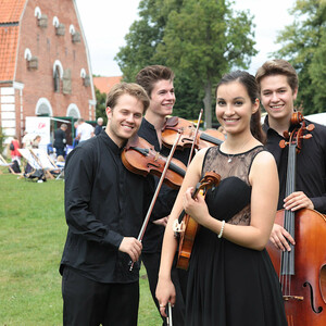 Ein Streichquartett in schwarzer Kleidung spielt im Freien vor einem Backsteingebäude.