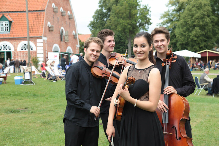 Ein Streichquartett in schwarzer Kleidung spielt im Freien vor einem Backsteingebäude.