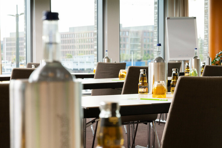 Heller Tagungsraum mit Tischen, Stühlen, Wasserflaschen, Apfelsaft und Flipchart im ATLANTIC Hotel Kiel.