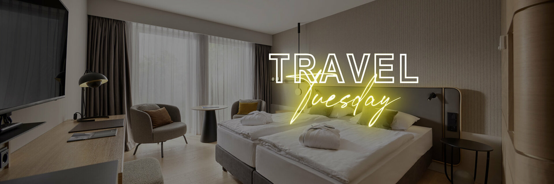 Modern hotel room with double bed, desk, armchair and large windows, text "Travel Tuesday" in neon.