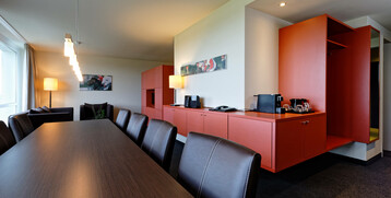 Modern conference room with long table, leather armchairs, red sideboard and coffee machine at the ATLANTIC Hotel Galopprennbahn.