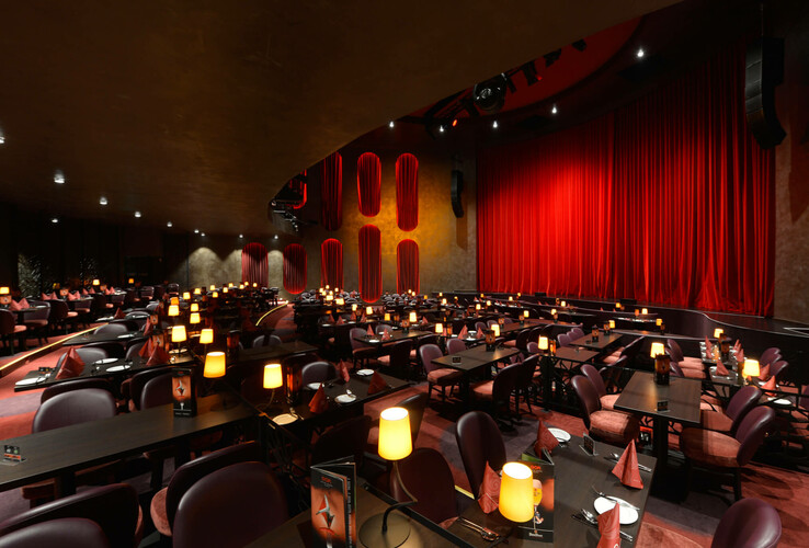 Elegantes Hotelrestaurant mit gedämpfter Beleuchtung, roten Vorhängen und gedeckten Tischen für ein stilvolles Ambiente.