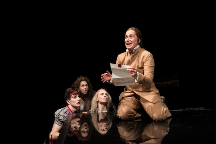 Four people in a theater scene, one kneels with a letter, the others look on intently. © bremer shakespeare company