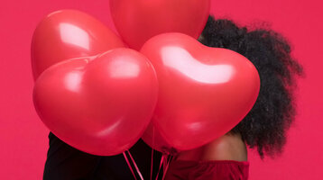 Couple hugging behind red heart balloons against a red background.
