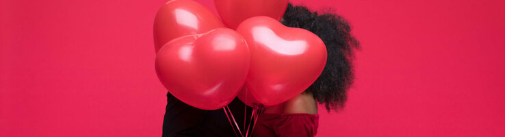 Paar umarmt sich hinter roten Herzluftballons vor rotem Hintergrund.