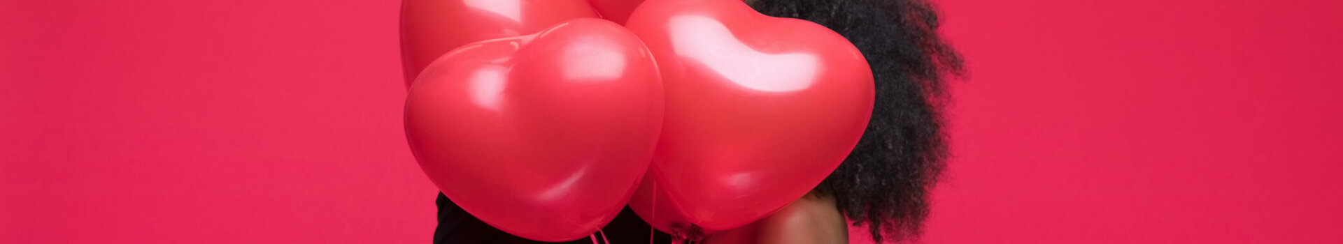Couple hugging behind red heart balloons against a red background.