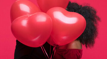 Paar umarmt sich hinter roten Herzluftballons vor rotem Hintergrund.