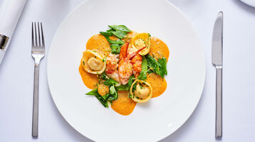 Das Restaurant alto im ATLANTIC Grand Hotel Bremen Elegantes Gericht mit Hummer, Ravioli und grünen Blättern auf orangener Sauce, serviert auf weißem Teller.