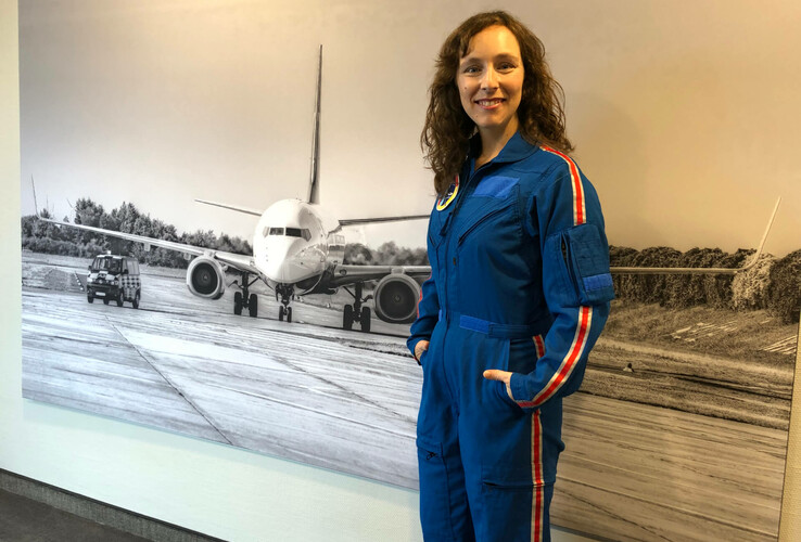 Frau in blauem Fluganzug vor einem großen Schwarz-Weiß-Foto eines Flugzeugs auf einer Landebahn.