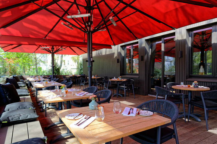 Restaurant CHALET at the ATLANTIC Hotel Landgut Horn Sunny terrace with wooden tables and red parasols, set for guests at the ATLANTIC Hotel Landgut Horn Bremen.