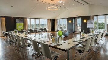 Die Roof Lounge mit umlaufender Dachterrasse läd zu Meetings und privaten oder geschäftlichen Feierlichkeiten ein Heller Konferenzraum im ATLANTIC Hotel Lübeck mit U-förmiger Bestuhlung, großen Fenstern und moderner Beleuchtung.