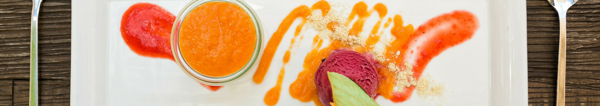 Dessertvariation Elegantes Dessert auf rechteckigem Teller mit Fruchtpüree, Sorbet und Garnitur, auf Holztisch serviert.