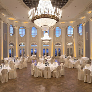 Eleganter Ballsaal mit runden, weiß gedeckten Tischen, hohen Fenstern und großen Kronleuchtern im ATLANTIC Grand Hotel Travemünde.