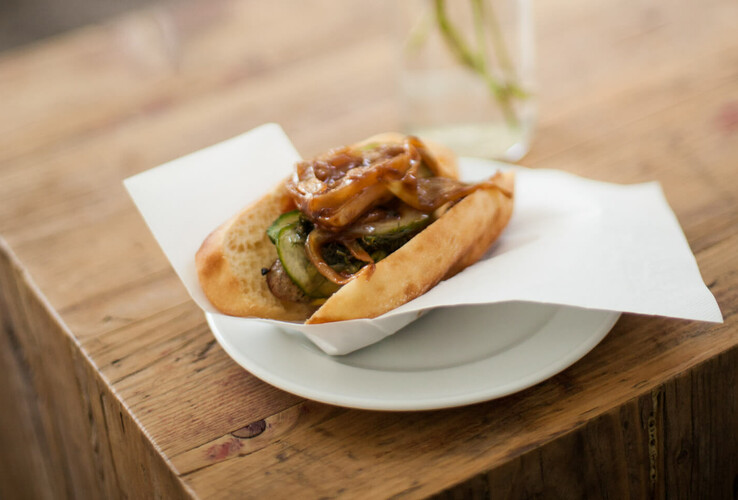Hotdog with grilled vegetables and onions on a plate, served on a wooden table at the ATLANTIC Hotel Airport Bremen.