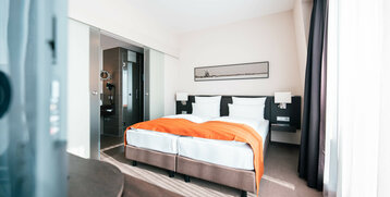 Helles Hotelzimmer mit Doppelbett, orangefarbener Decke, modernem Bad und großem Fenster im ATLANTIC Hotel Lübeck.