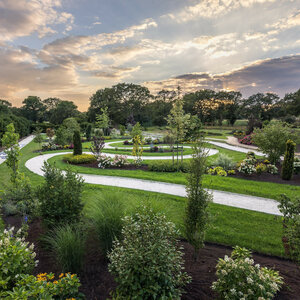 Geschwungene Gartenwege durch blühende Beete und grüne Rasenflächen bei Sonnenuntergang.