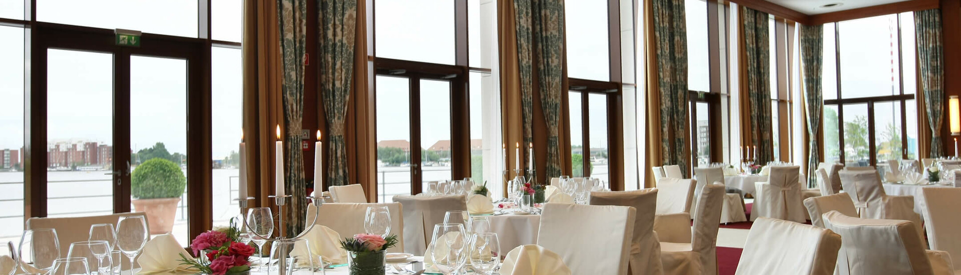Set tables in the banquet hall Wilhelmshaven Elegant banquet hall in the ATLANTIC Hotel Wilhelmshaven with set tables and large windows overlooking the water.