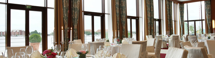 Eleganter Bankettsaal im ATLANTIC Hotel Wilhelmshaven mit gedeckten Tischen und großen Fenstern mit Blick auf das Wasser.