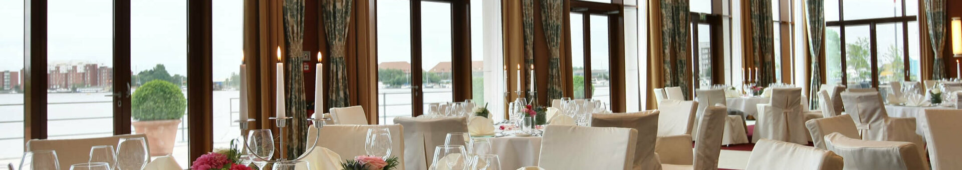 Set tables in the banquet hall Wilhelmshaven Elegant banquet hall in the ATLANTIC Hotel Wilhelmshaven with set tables and large windows overlooking the water.