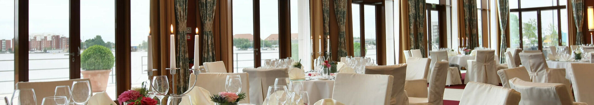 Eleganter Bankettsaal im ATLANTIC Hotel Wilhelmshaven mit gedeckten Tischen und großen Fenstern mit Blick auf das Wasser.