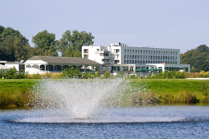 Water feature on the lake in front of the ATLANTIC Hotel Galopprennbahn in Bremen ATLANTIC Hotel Galopprennbahn with fountain in the foreground, surrounded by green landscape and trees.