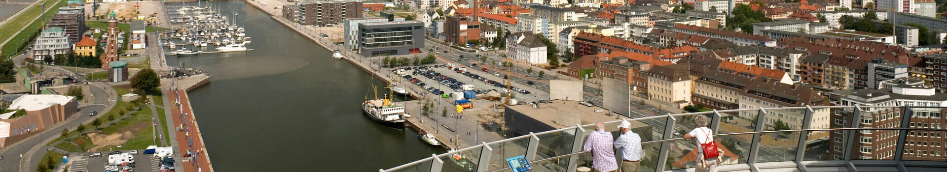 Blick von ATLANTIC Hotel Sail City auf Bremerhavens Hafen und Stadt bei klarem Himmel, mit Besuchern auf der Aussichtsplattform.
