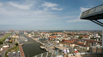 View from ATLANTIC Hotel Sail City of Bremerhaven's harbor and city under a clear sky, with visitors on the viewing platform.