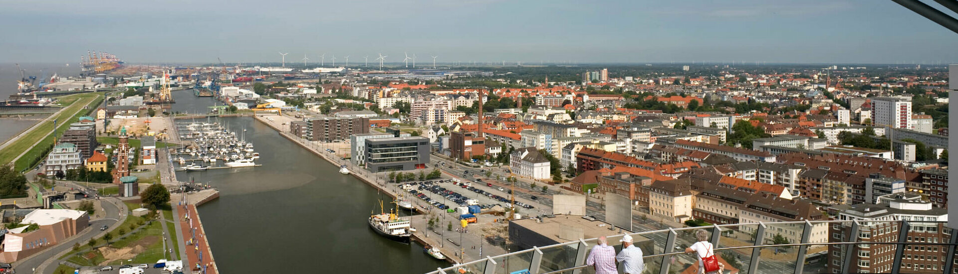 Blick von ATLANTIC Hotel Sail City auf Bremerhavens Hafen und Stadt bei klarem Himmel, mit Besuchern auf der Aussichtsplattform.