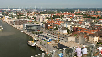 Blick von ATLANTIC Hotel Sail City auf Bremerhavens Hafen und Stadt bei klarem Himmel, mit Besuchern auf der Aussichtsplattform.