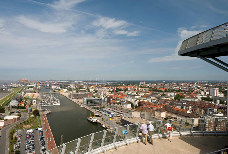 View from ATLANTIC Hotel Sail City of Bremerhaven's harbor and city under a clear sky, with visitors on the viewing platform.