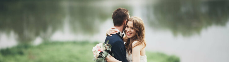 Heiraten am Universum | ATLANTIC Hotel Universum Bremen Ein Brautpaar umarmt sich vor einem See im Grünen, die Braut hält einen Blumenstrauß.